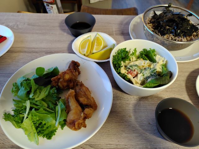 コンドの食事、スーパーで買った唐揚げとマカロニサラダ、日本から持ち込んだそばをテーブルに並べたところを撮影した写真